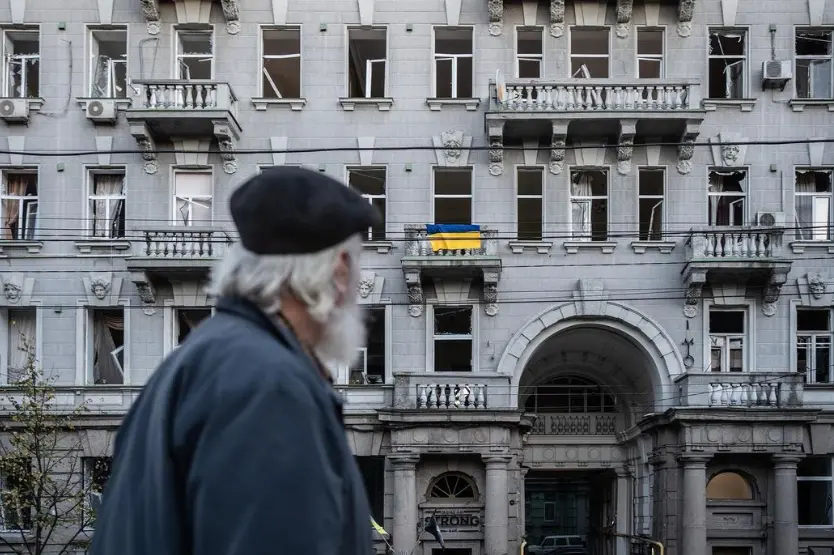 Чоловік дивиться на пошкоджений внаслідок обстрілів будинок. На одному з балконів — український стяг | Фото: Сергій Коровайний