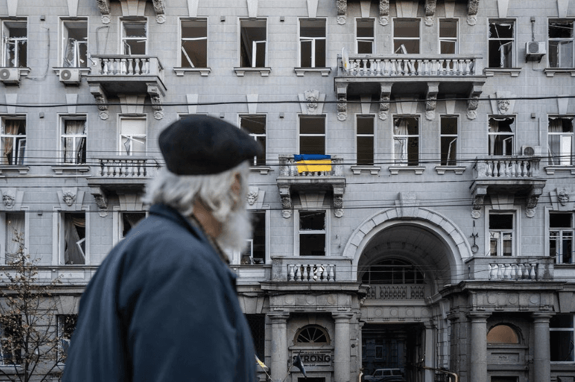 Чоловік дивиться на пошкоджений внаслідок обстрілів будинок. На одному з балконів — український стяг | Фото: Сергій Коровайний