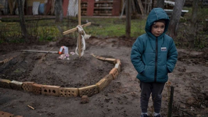 Хлопчик стоїть біля могили мами, вбитої окупантами на Київщині. Фото AP